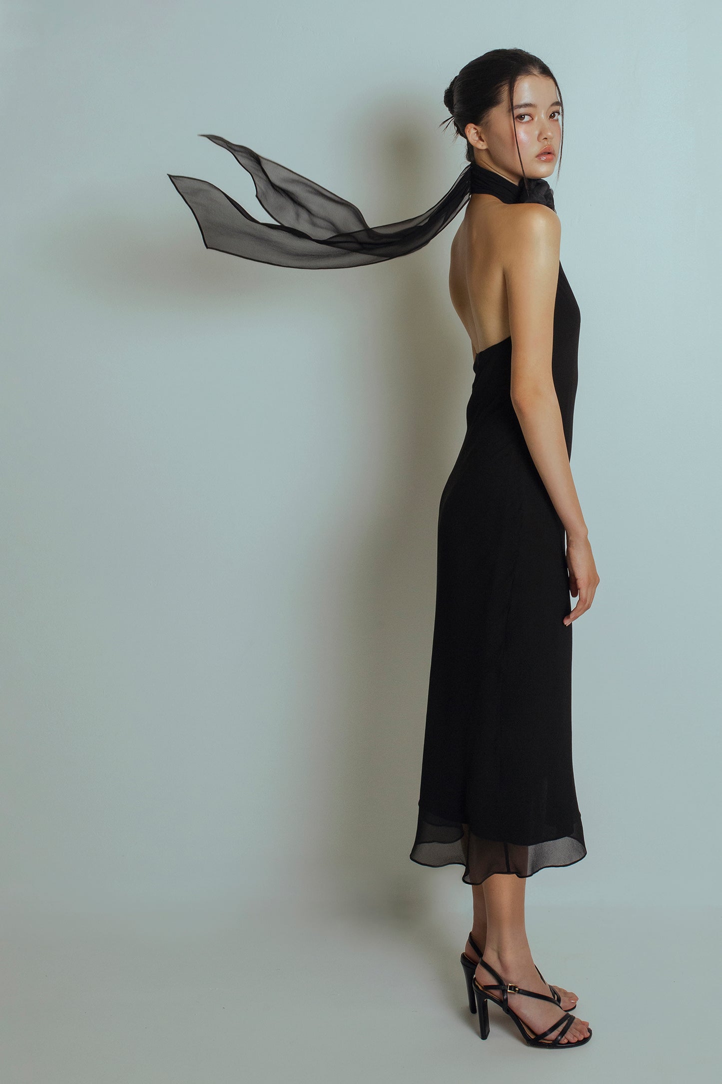 Side view of Black midi length dress with a detachable flower brooch at front neckband, bare back and flowing ties at the back neckband