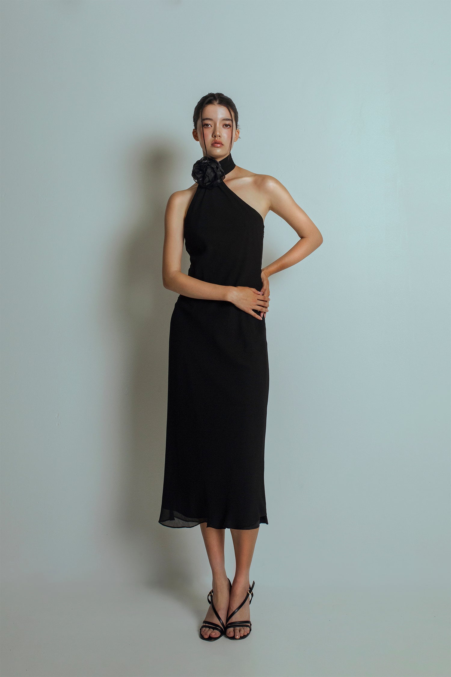 Front view of Black midi length dress with an asymmetrical neckline and a detachable flower brooch at neckband