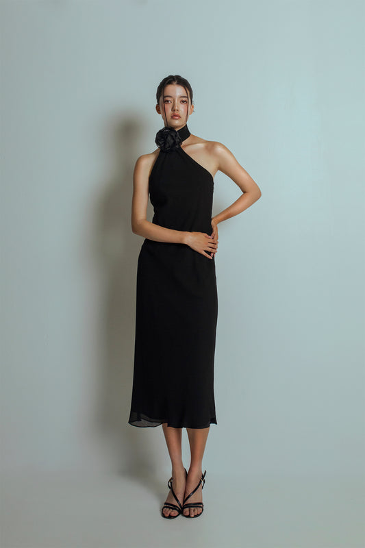 Front view of Black midi length dress with an asymmetrical neckline and a detachable flower brooch at neckband