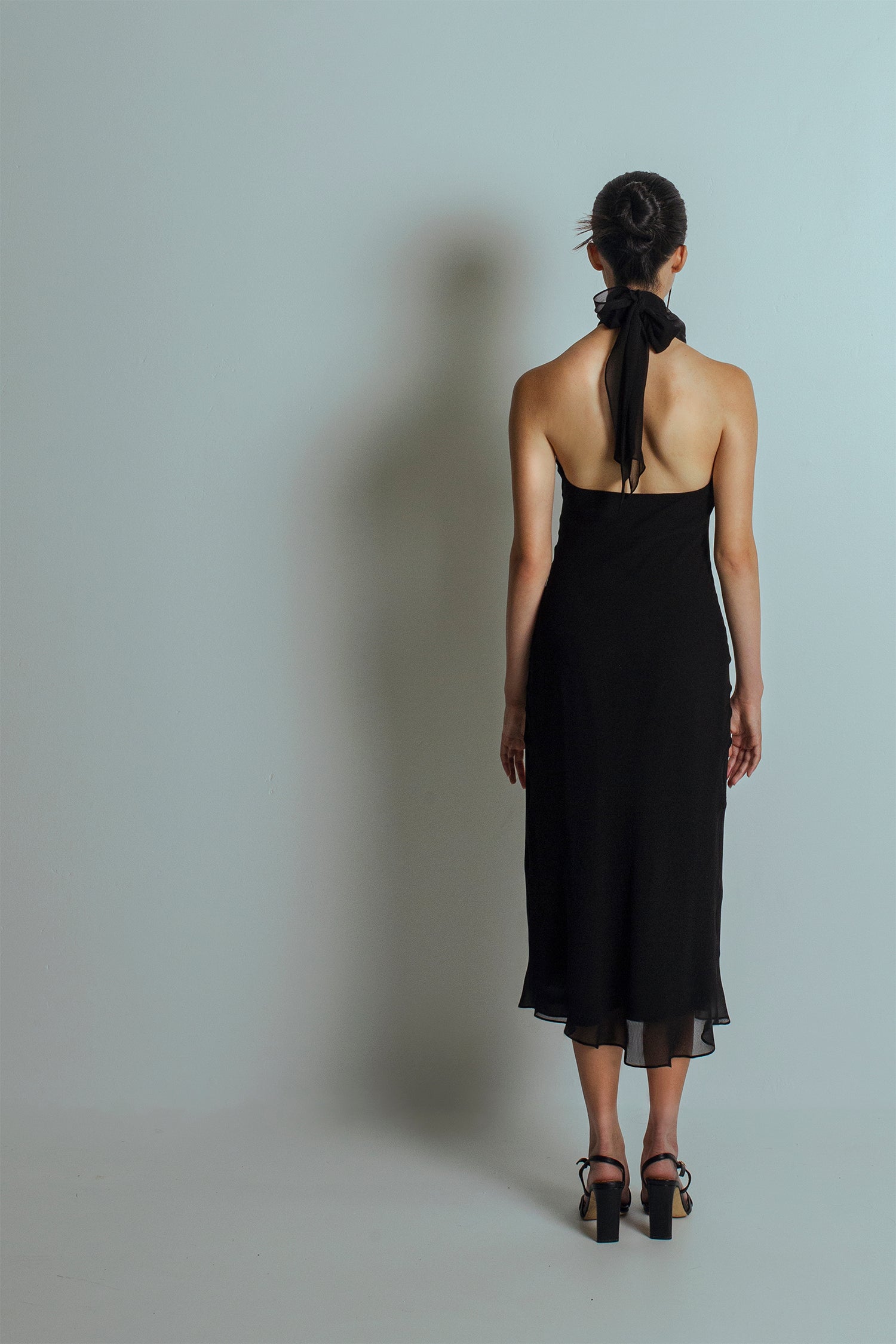 Back view of Black midi length dress with bare back and flowing ties at the neckband