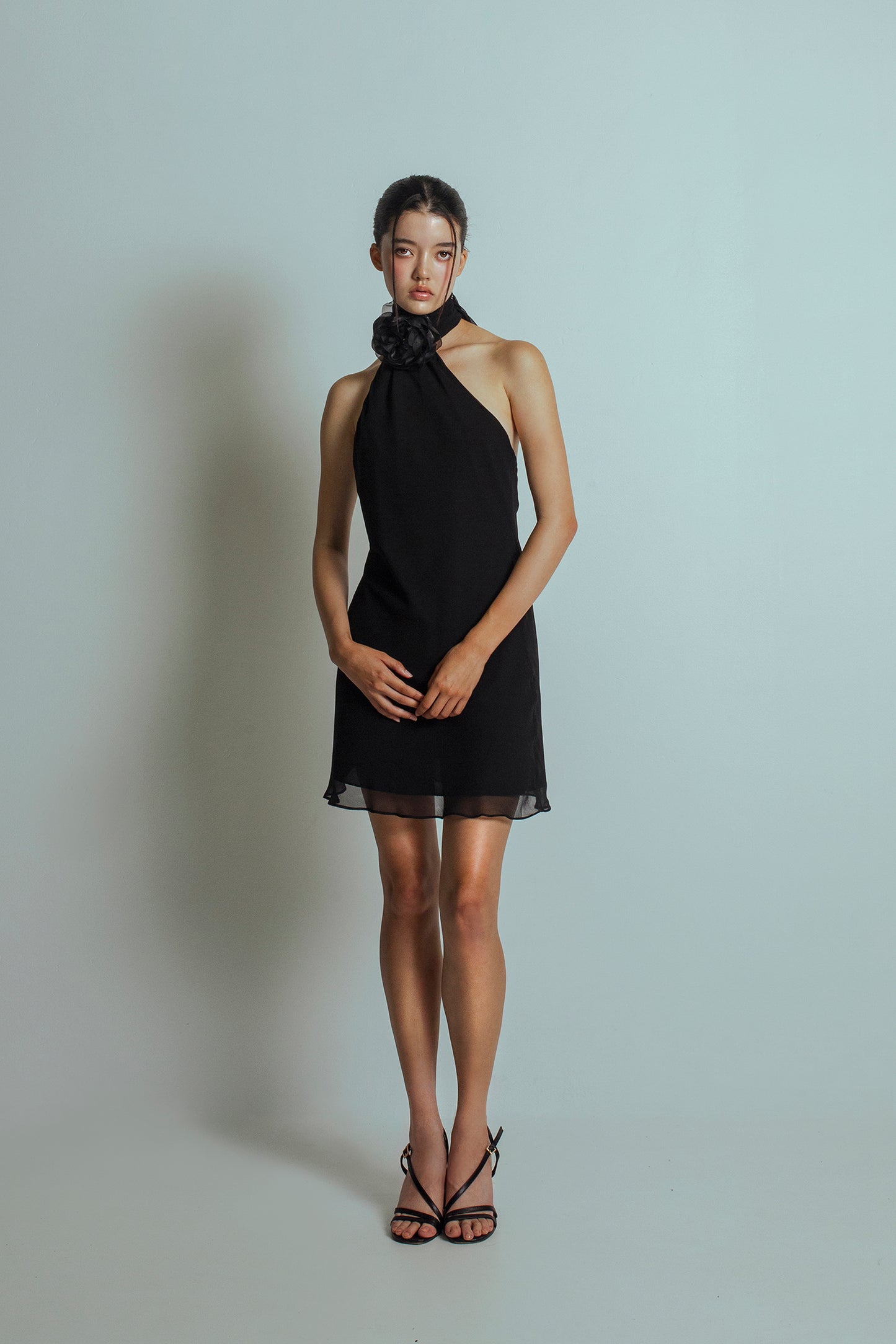 Front view of Black mini length dress with an asymmetrical neckline and a detachable flower brooch at neckband