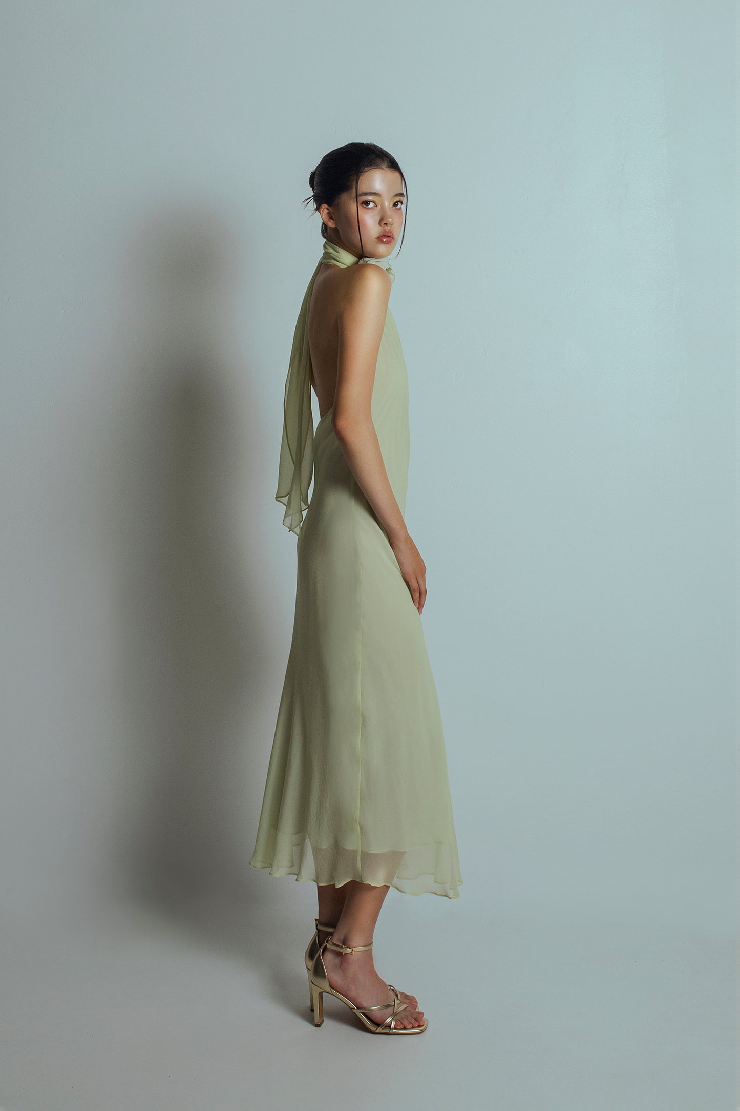 Side view of Celadon green midi length dress with bare back and flowing ties at the back neckband