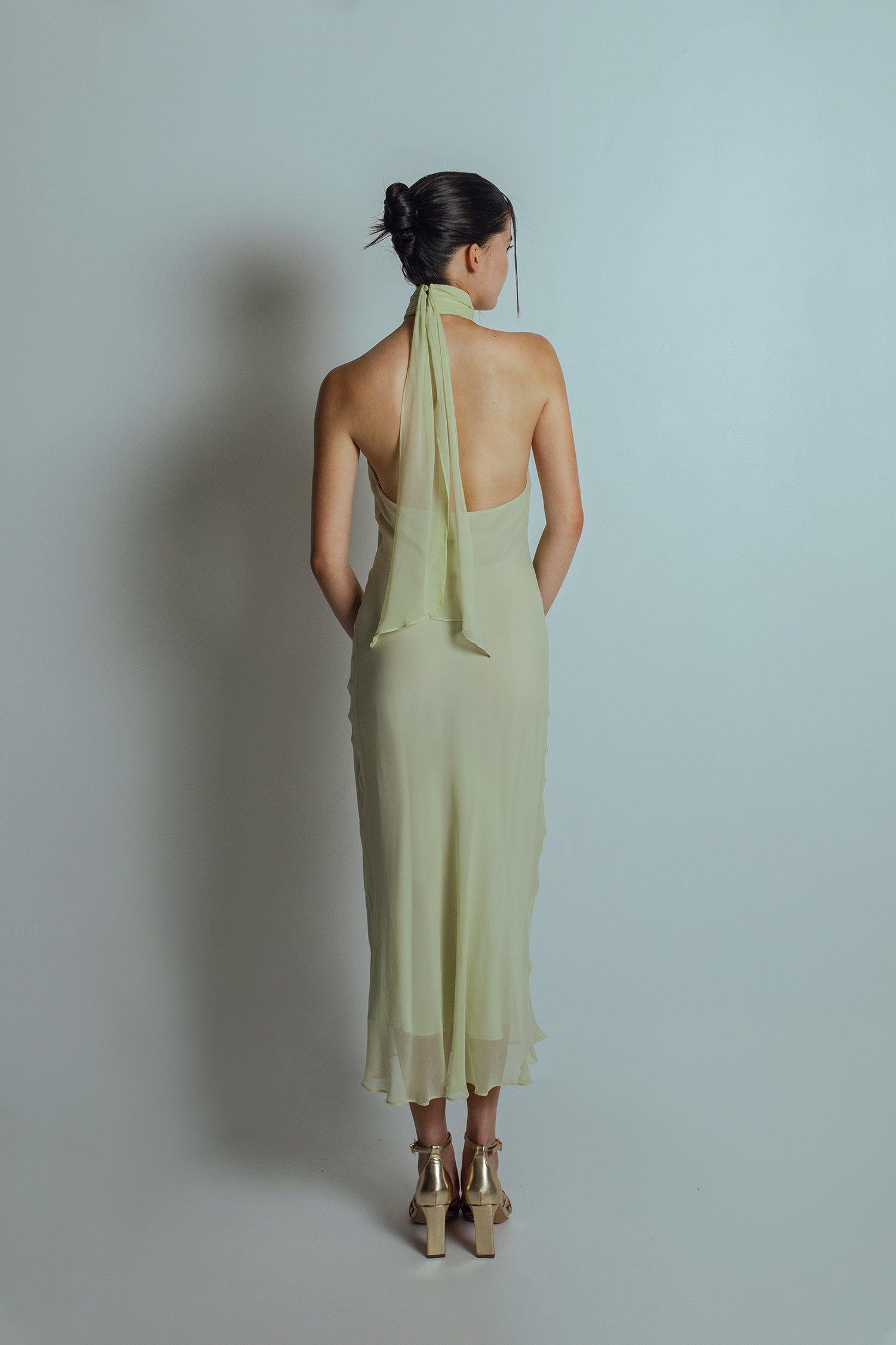 Back view of Celadon green midi length dress with bare back and flowing ties at the neckband
