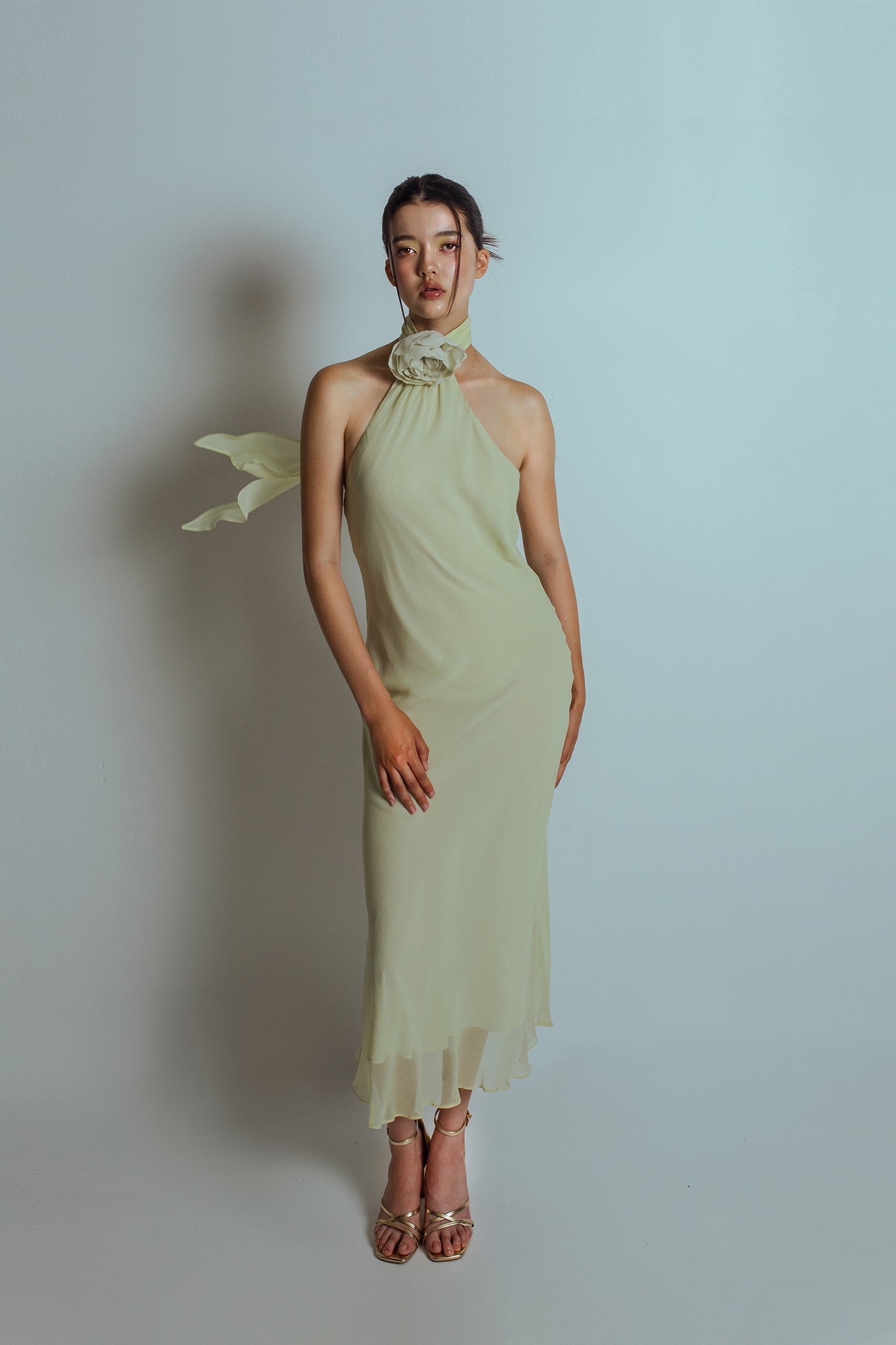 Front view of Celadon green midi length dress with an asymmetrical neckline and a detachable flower brooch at neckband