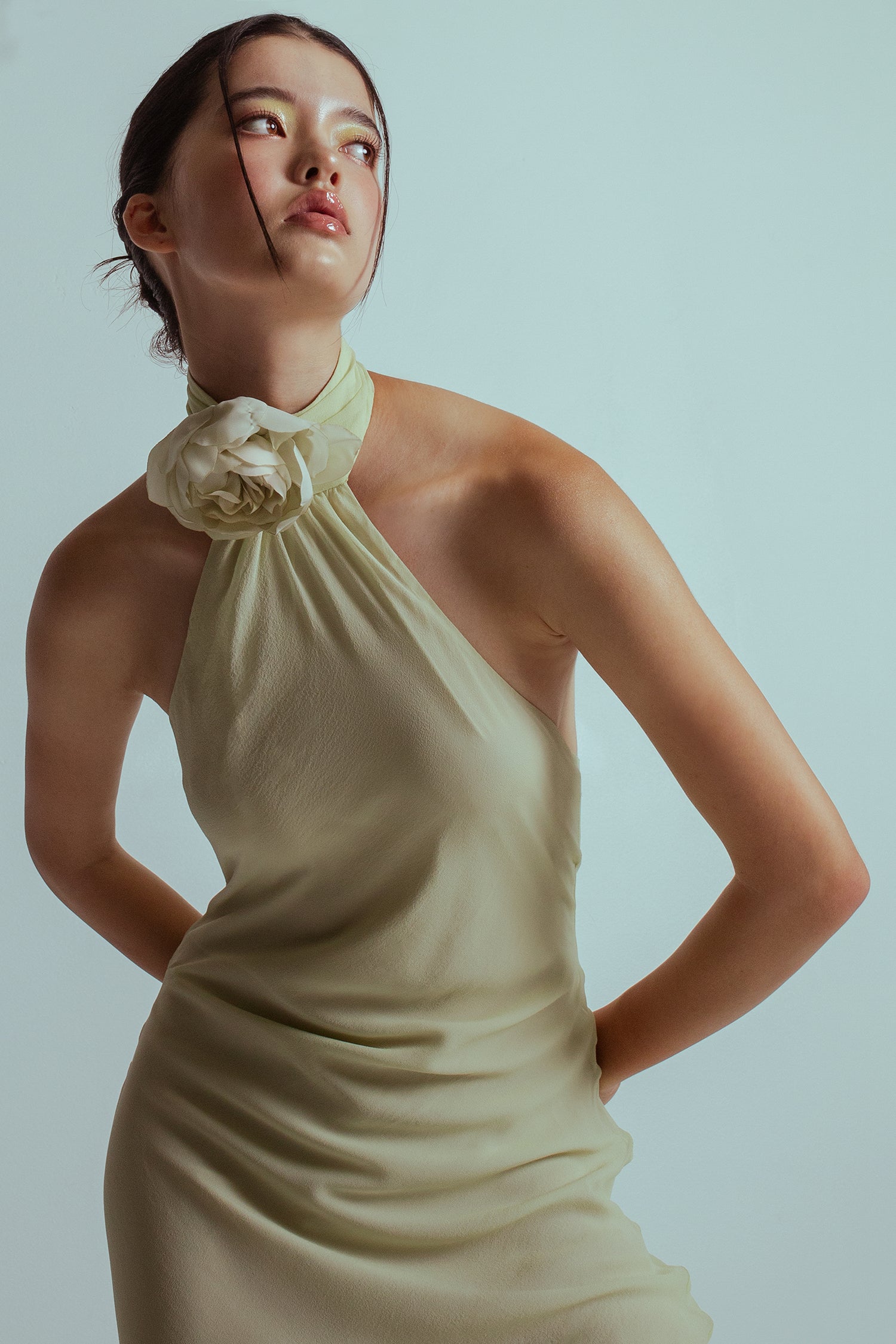 Half cropped image of model wearing a Celadon green midi length dress with an asymmetrical neckline and a detachable flower brooch at neckband