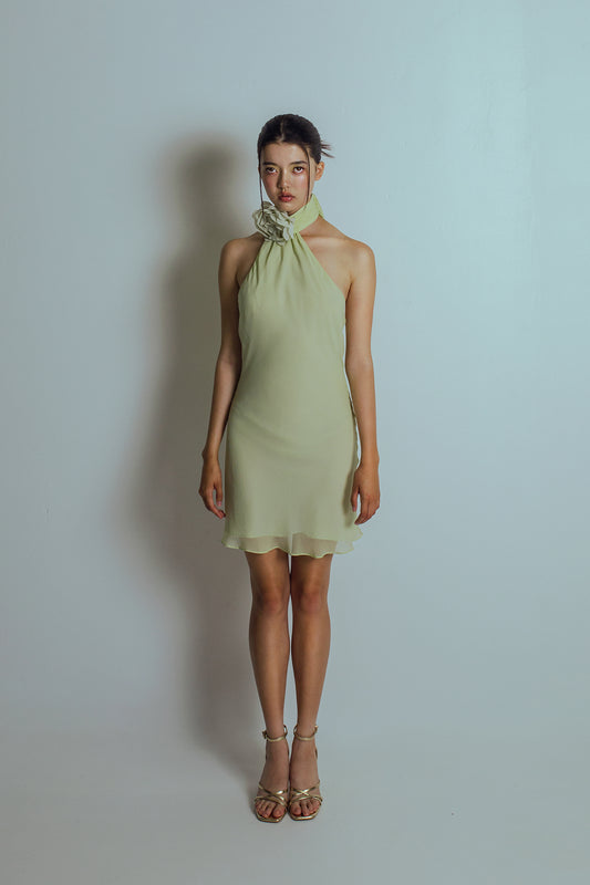Front view of Celadon green mini length dress with an asymmetrical neckline and a detachable flower brooch at neckband