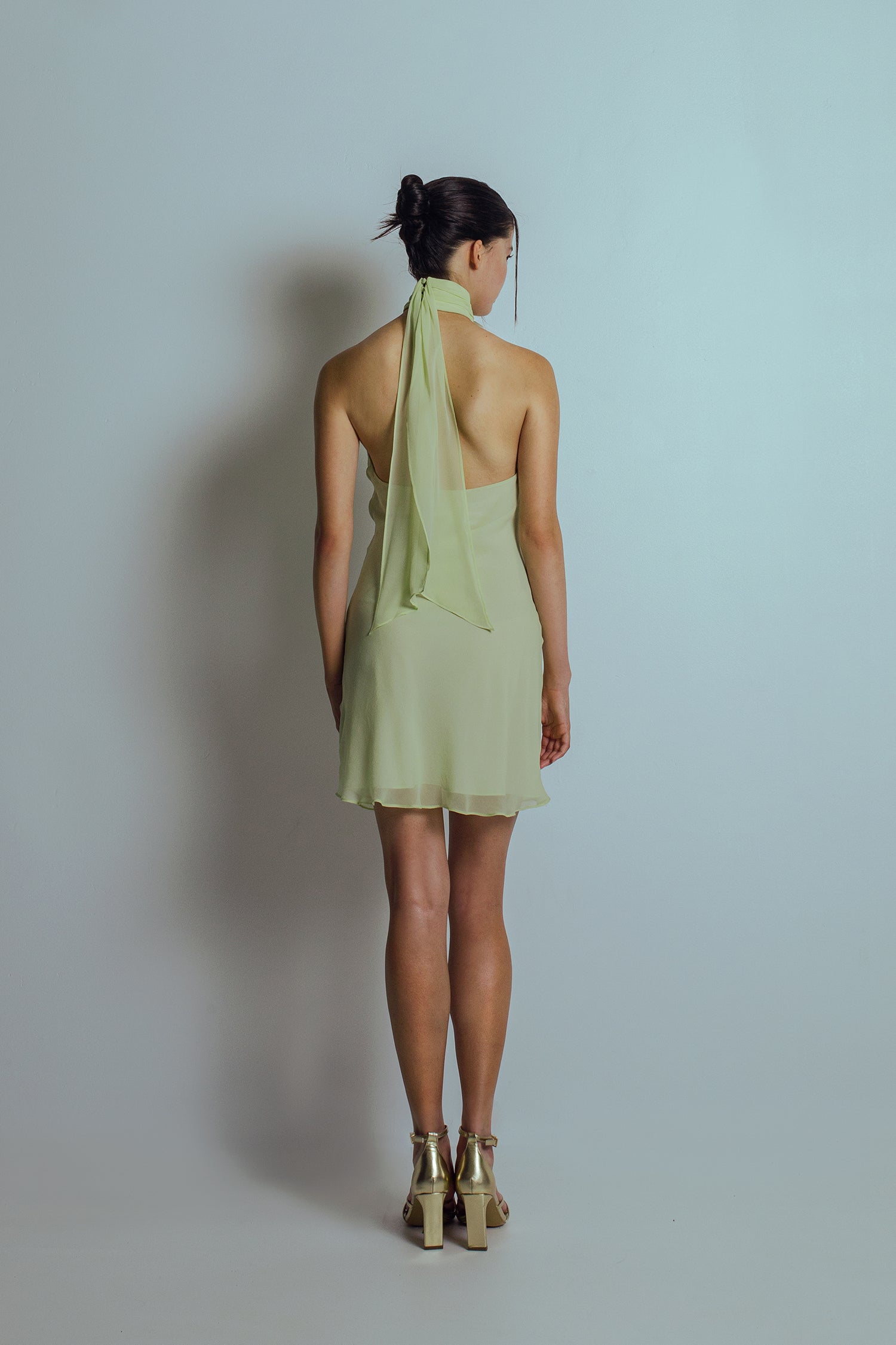 Back view of Celadon green mini length dress with bare back and flowing ties at the neckband